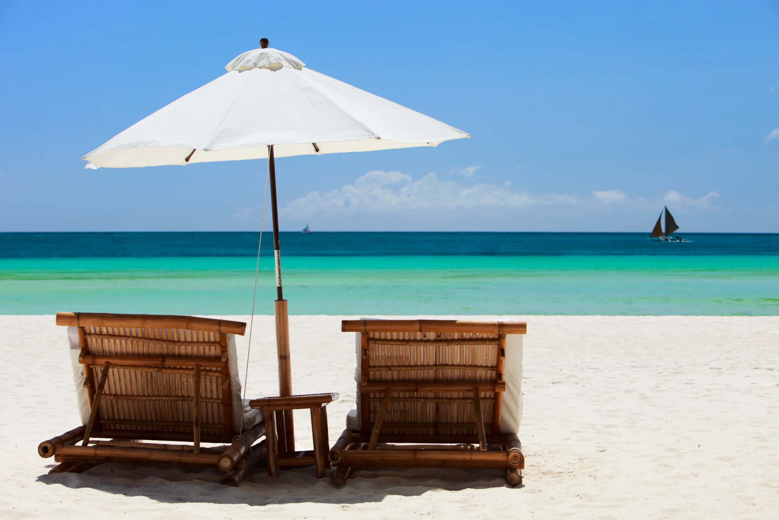 Deux chaises longues sous un parasol blanc sur une plage de sable fin avec mer turquoise