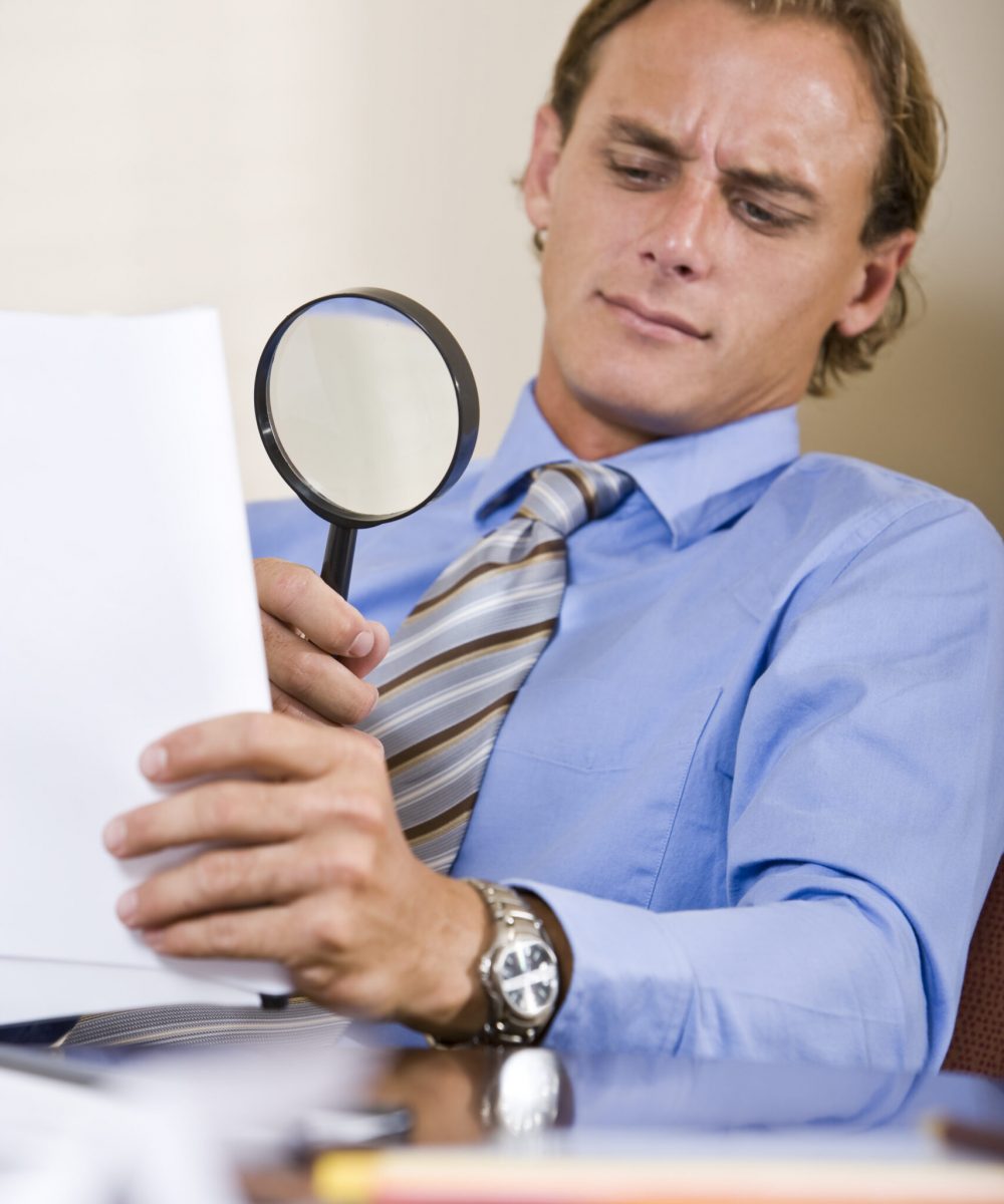 Businessman reading fine print in contract with magnifying glass